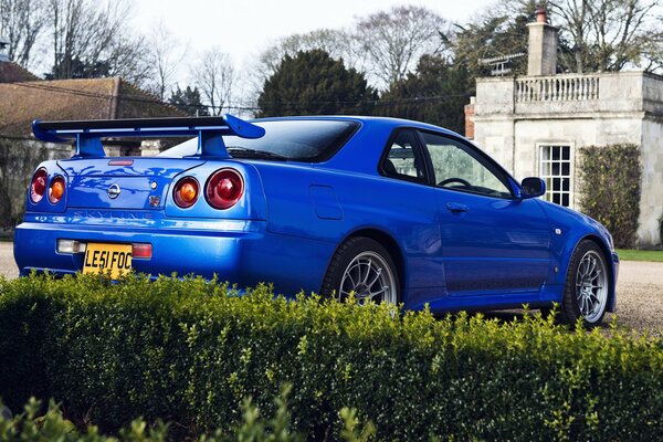 Blue Nissan near green bushes on the background of an old house