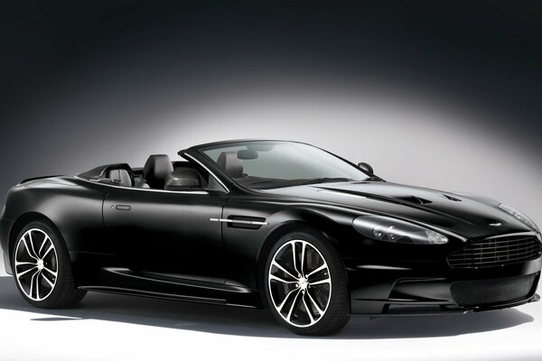A black Aston Martin convertible on a gray background is illuminated with white light