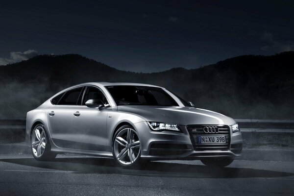 Audi A7 gris sobre un fondo oscuro con montañas