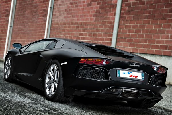 Lamborghini noir mat près du mur de briques