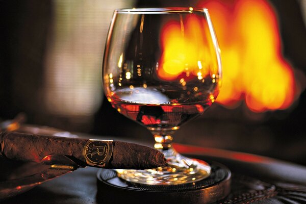 A glass of cognac and a cigar on the background of the fireplace