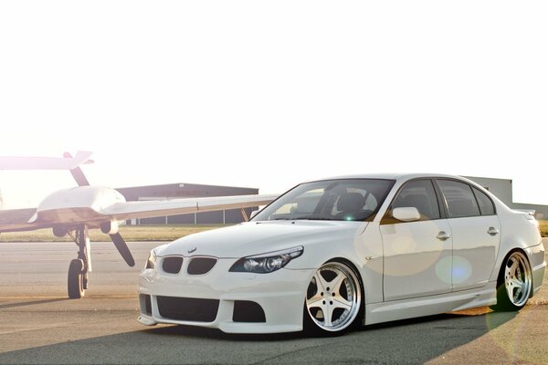 A beautiful white car m5, e60 stands at the airfield next to the corn plane