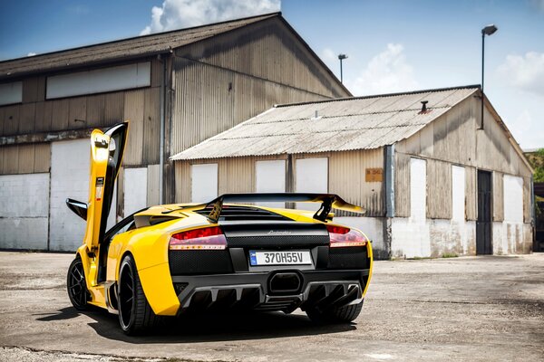 Żółte Lamborghini z otwartymi drzwiami na tle starego magazynu