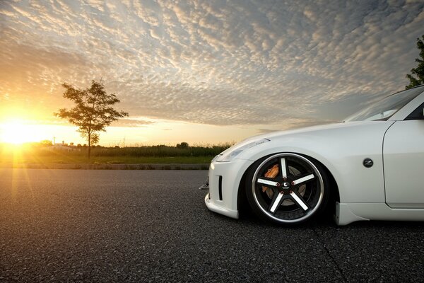 Blanco discreto Nissan 350Z en el fondo de una hermosa puesta de sol