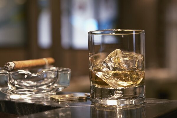 Whisky con hielo y cigarro en un cenicero de vidrio