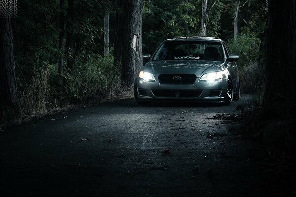 Subaru viaja por la noche con los faros encendidos en el camino forestal