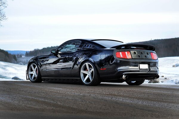 Ford Mustang negro en la carretera de invierno