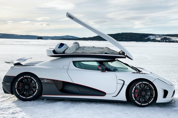A white sports car with a pilot lying on the roof is standing in the snow