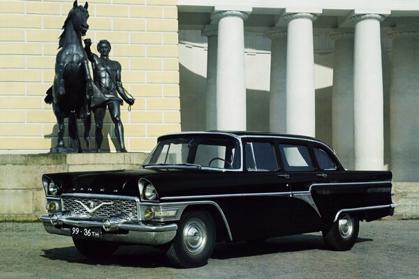 A black car next to a statue of a man with a horse