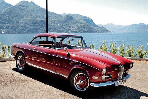 Roter Bmw 1956 auf dem Hintergrund der Berge und des Flusses