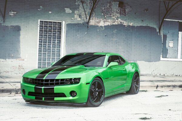 A green Chevrolet near a dilapidated building