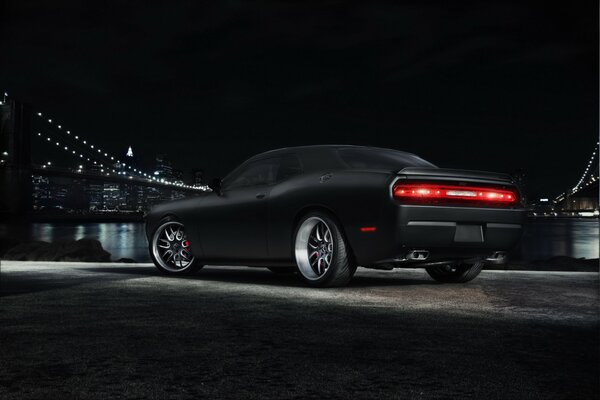 Dodge Challenger negro en el fondo de una metrópolis con un puente