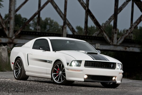 Une Ford Mustang blanche passe devant le pont