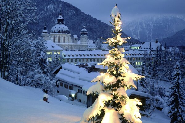 Weihnachtsbaum mit Hintergrundbeleuchtung auf dem Hintergrund der verschneiten Stadt