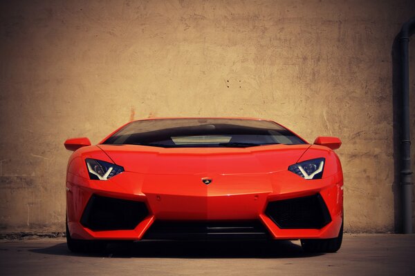 A red Lamborghini aventador stands against a wall