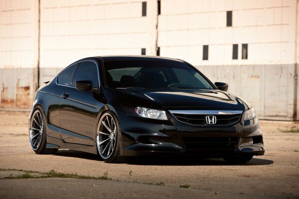 A black Honda stands on concrete against the background of a white building