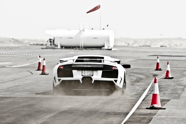 A white Lamborghini on the race track is flying raising dust