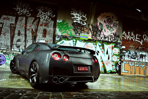 Nissan gris se para contra la pared con graffiti