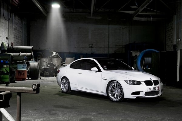 Une BMW blanche se tient dans un garage sombre