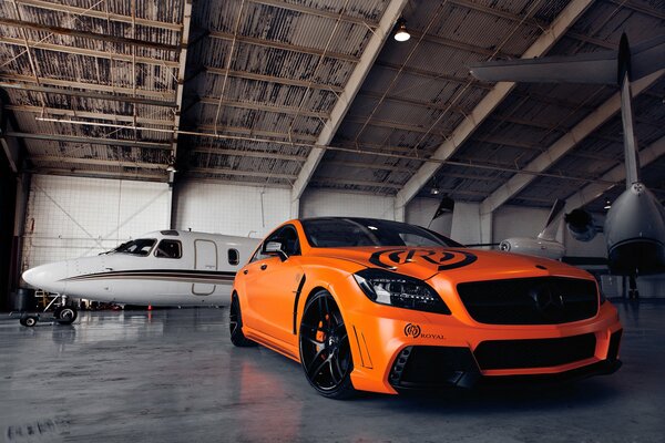Mercedes naranja en un hangar de aviones con un avión
