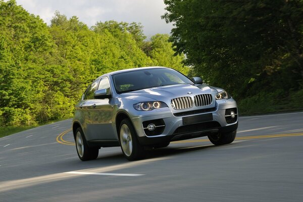 BMW x6 fährt auf der Straße in der Nähe von Bäumen