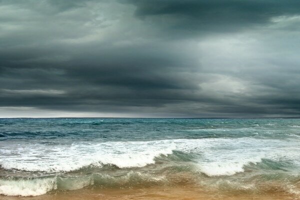 The sea splashes waves on the sand in a thunderstorm