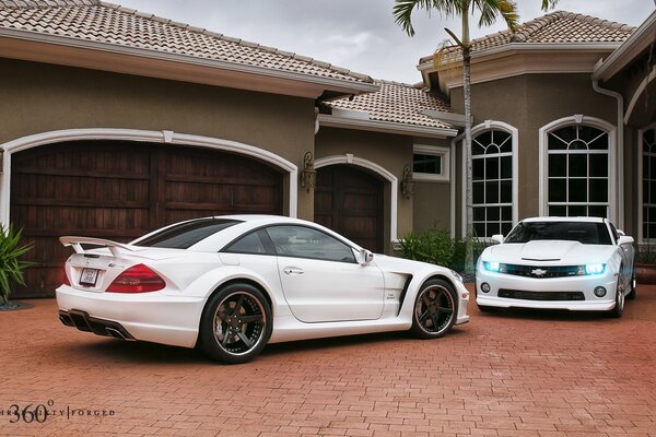 Der Muscle Car Camaro und der elegante Mercedes stehen neben dem Haus