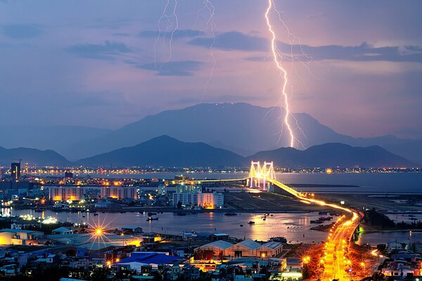 A city with a sea in the distance mountains where lightning flashes