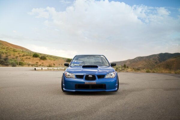 Subaru impreza azul en una carretera de concreto en el fondo de las colinas