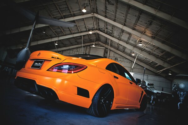 A chic tuned Mercedes-Benz in a hangar with an airplane