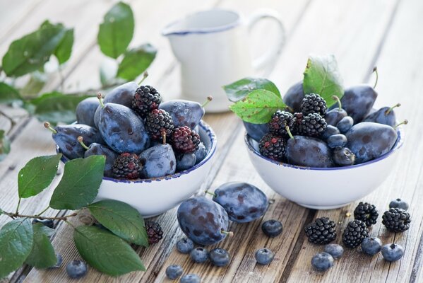 Nature morte de fruits violets mûres et prunes dans des tasses blanches