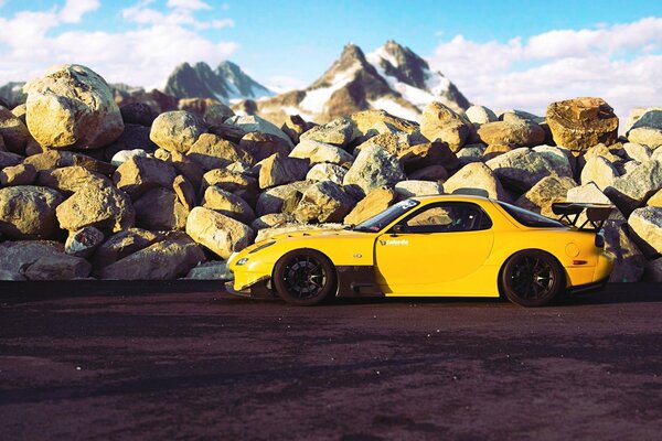 A tuned yellow Mazda on a platform in the mountains