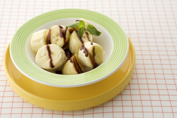 In a plate of banana with chocolate syrup and mint