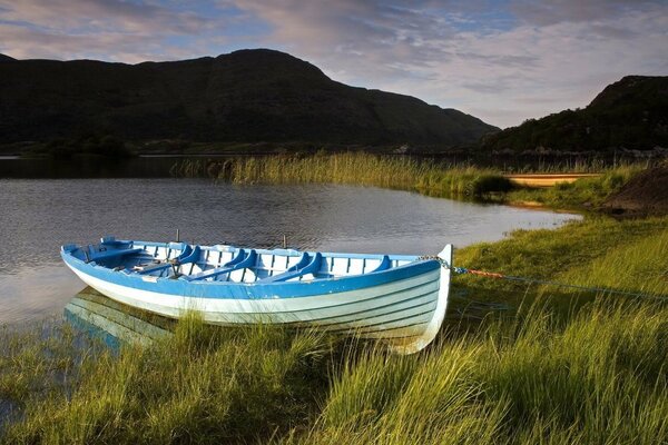 A neat blue-and-white boat docked on the shore of a mountain lake