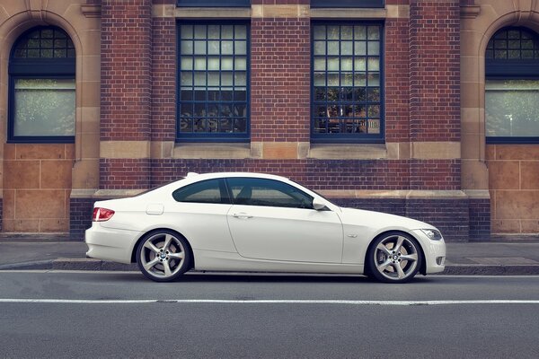 A white bmw is parked on the edge of the roadway against the background of a brick building