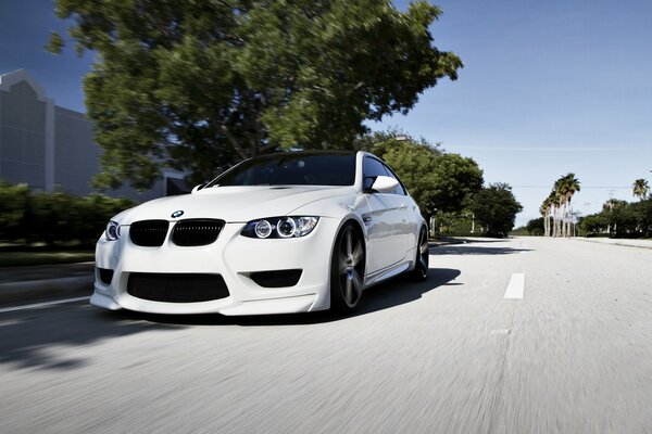 A white BMW is driving straight down the road