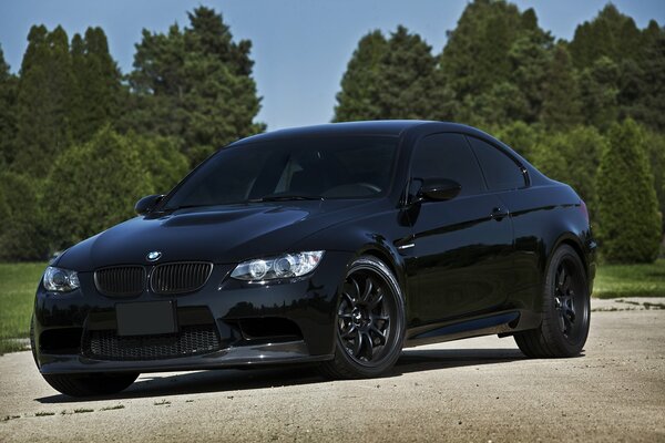 Shiny black tinted BMW on a background of blue sky and trees