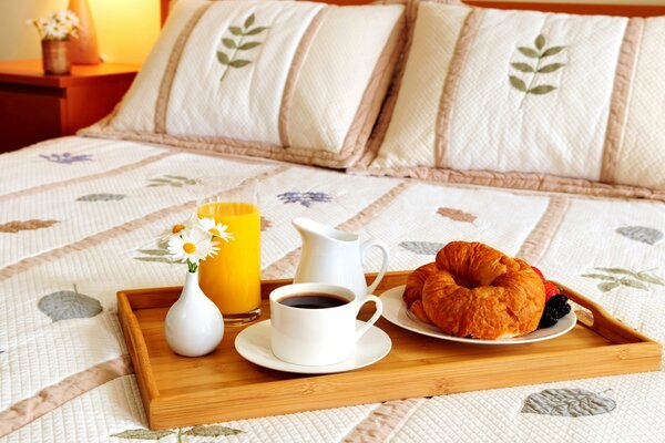 Tablett mit Café und Croissants und Gebäck auf dem Bett