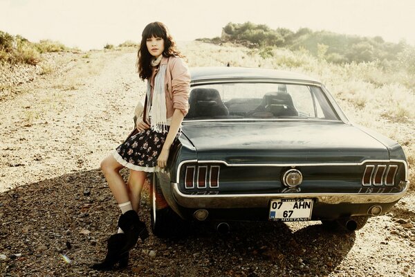 A brunette girl leaned on a retro mustang car