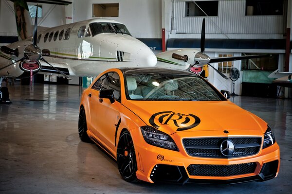 Orange Mercedes in an aircraft hangar on the background of a white plane