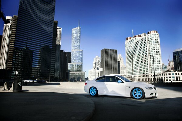 White car on blue alloy wheels on the background of urban high-rise buildings