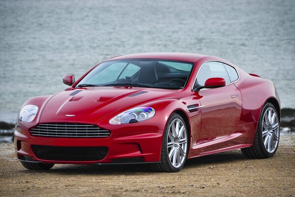Czerwony Aston Martin na piaszczystym brzegu morza