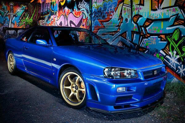 A blue Nissan parked near a graffiti wall