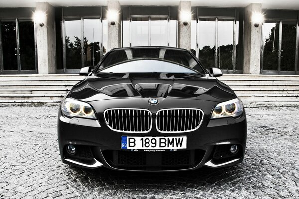 Glossy black BMW looks with headlights on the background of the building