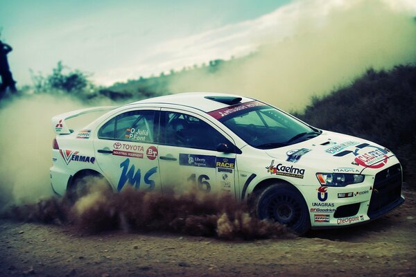 A white racing car with stickers passes a dusty track