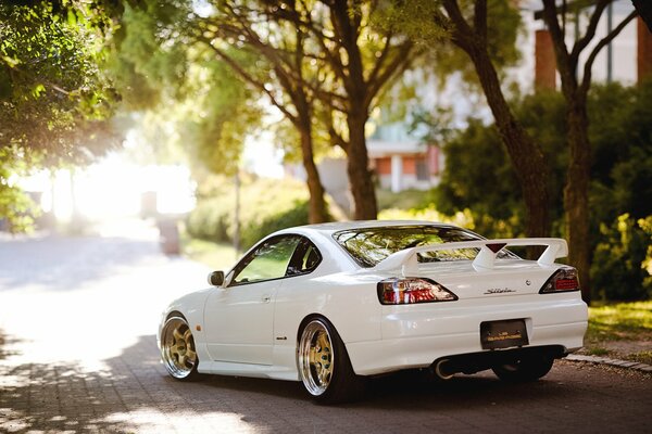 A white Nissan Silvia is driving around the city. Summer sunny day