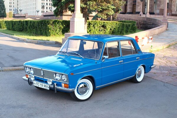 Soviet VAZ car on the background of a green lawn with a tree and a gray tall building and