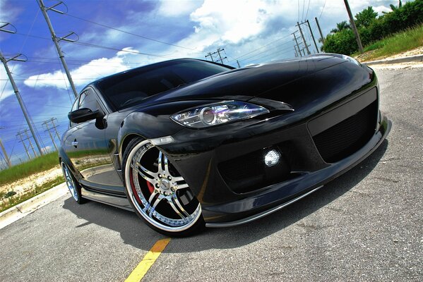 The front of a black sports car on the road against a background of blue sky and green grass