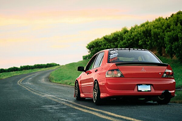 Mitsubishi Lancer rojo corre a lo largo de la carretera entre campos y árboles