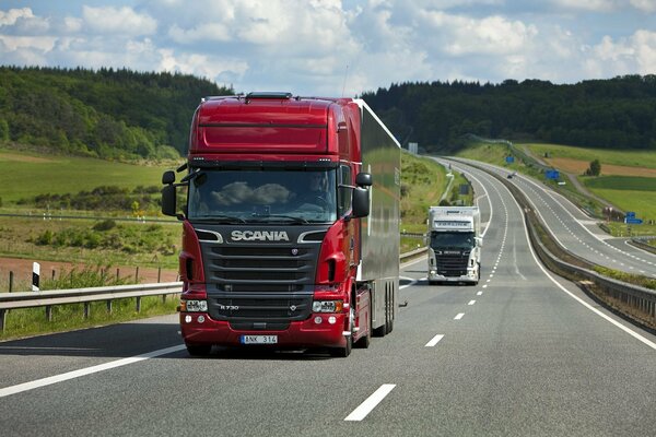 Красный грузовик Scania едет по шоссе. Летний пейзаж с полями